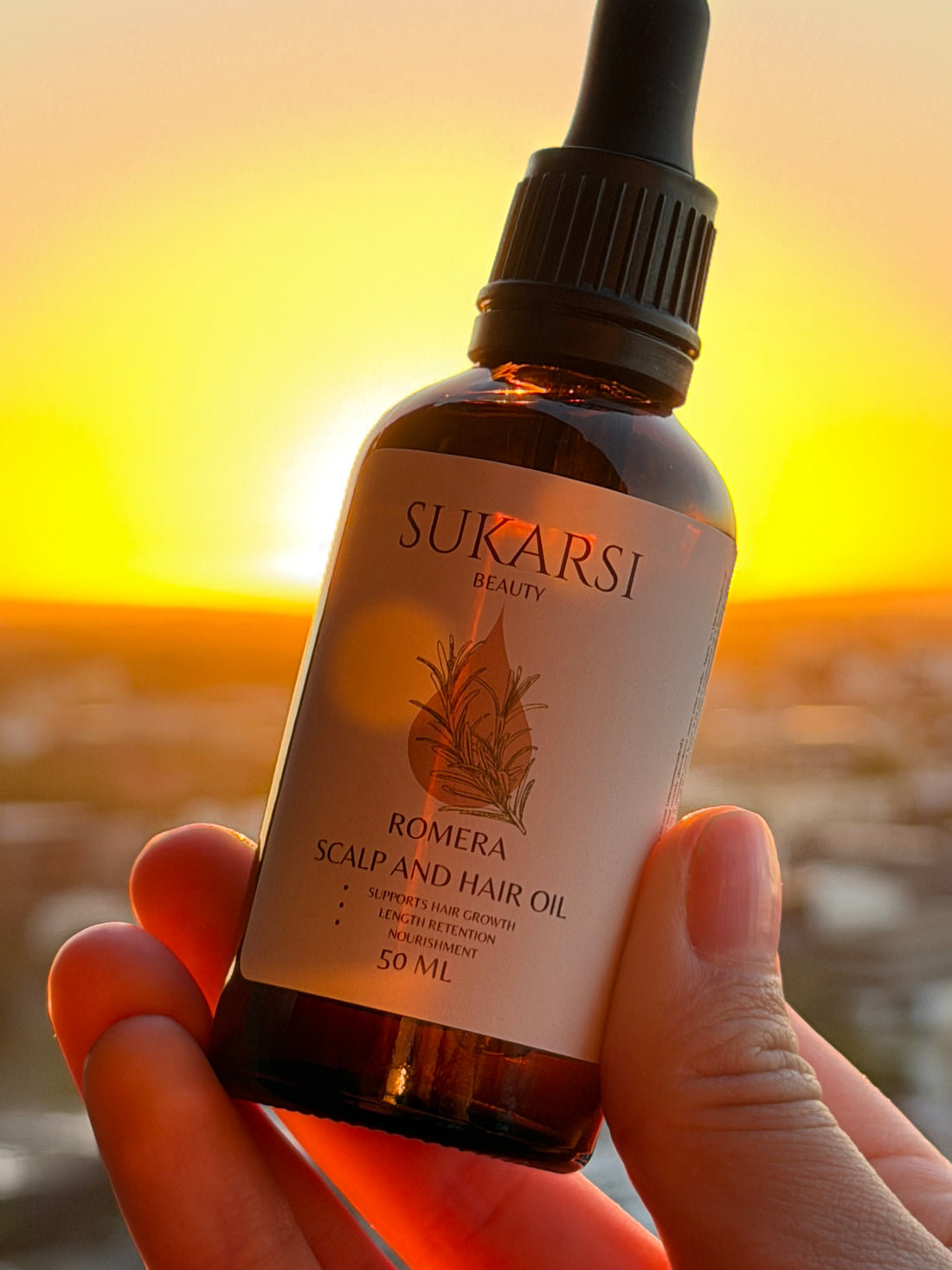 A hand holding Romera Scalp & Hair Oil against a sunset sky